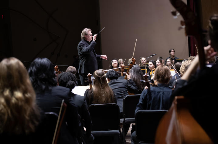 UK Symphony Orchestra Conductor leads an orchestra from the podium during a performance on stage.