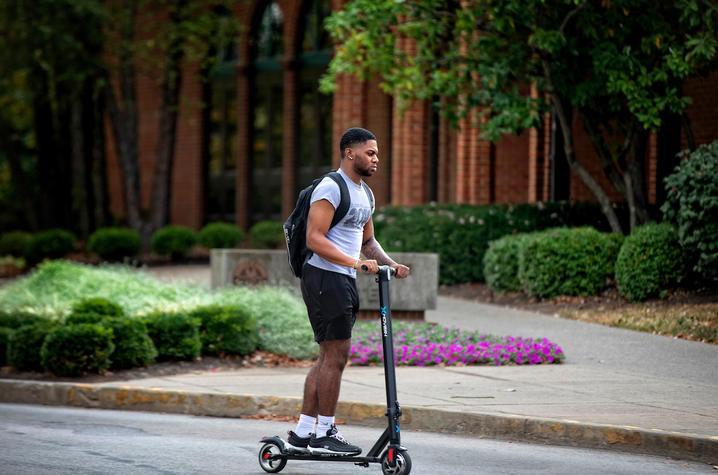 Photo of student riding scooter throughout campus