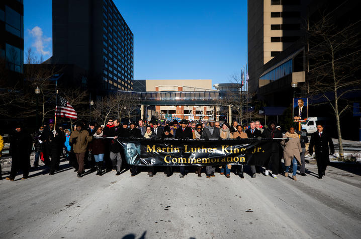 Large group marching on a snowy city street, holding a banner that reads “Martin Luther King Jr. Commemoration.”