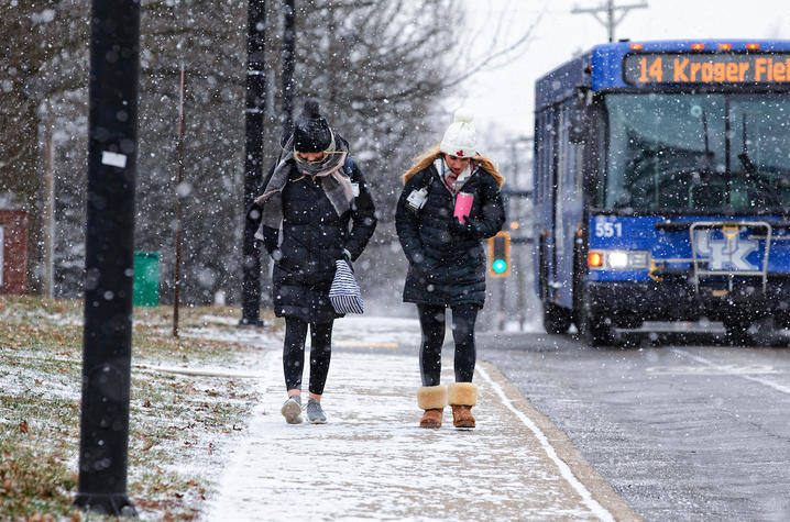 two students in the snow walking on a sidewalk next to a busy road
