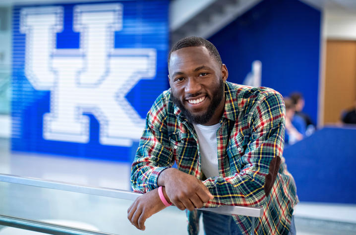 photo of Eli Caldwell leaning on glass railing in front of UK sign in student center