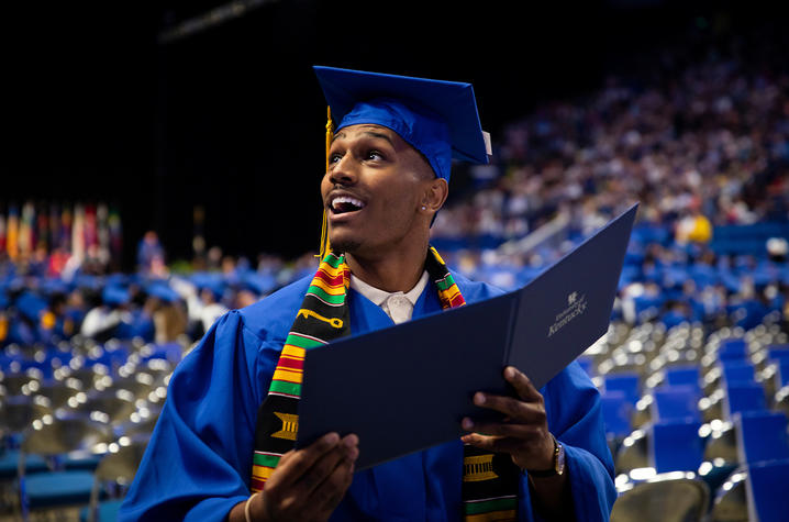 Male graduate in cap and gown holding diploma
