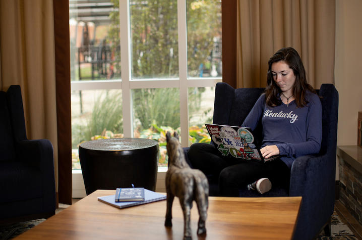 photo of student seated in comfy chair working on laptop near window of a den setting