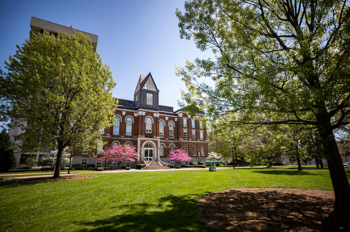 The Main Building at the University of Kentucky during springtime with blossoming trees and a light blue sky.