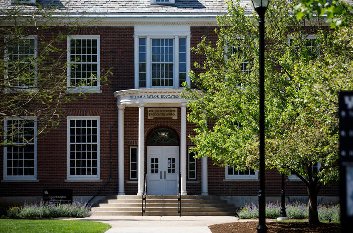 This is a front-view photo of the UK Taylor Education Building with trees and grass in sunlight in the foreground.