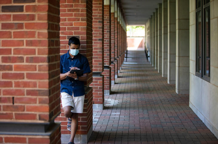 Student in mask against brick pillar