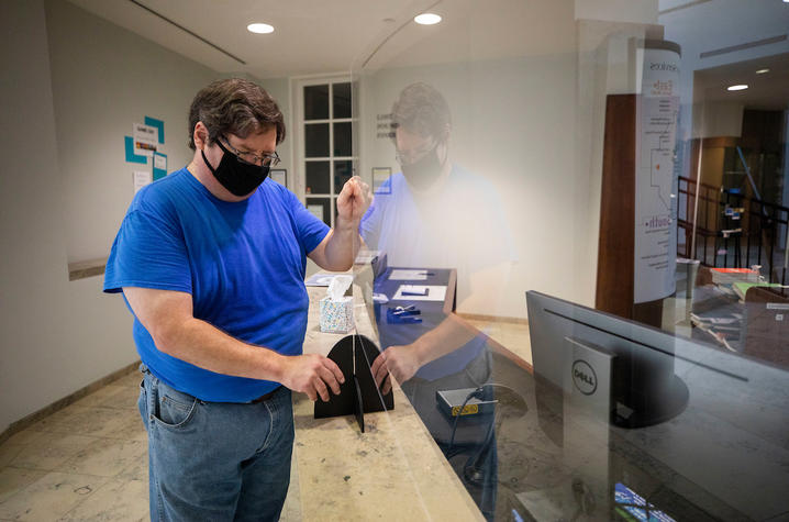 photo of employee installing plexiglass around the circulation desk at Young Library