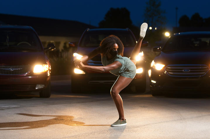 photo of "Once Vacant" dancer performing in parking lot with car lights shining behind her 