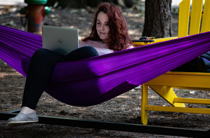 photo of student sitting in purple hammock, looking at laptop.