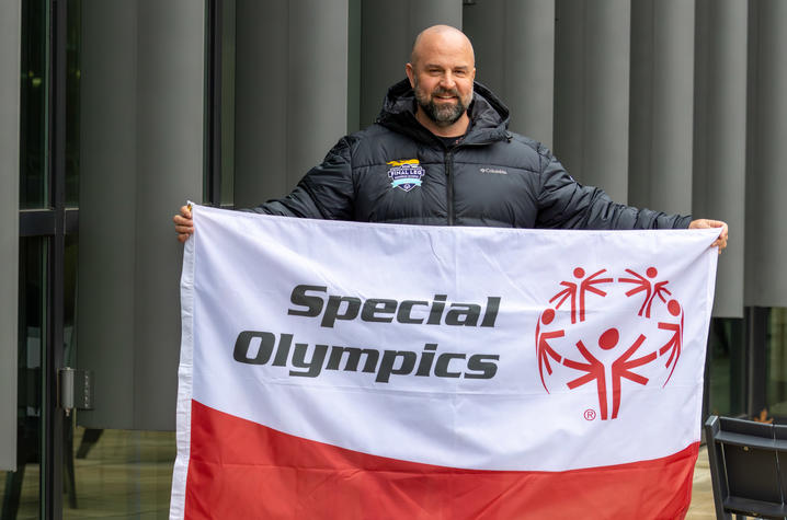 Capt. Adams standing, smiling, holding a Special Olympics flag in the student center