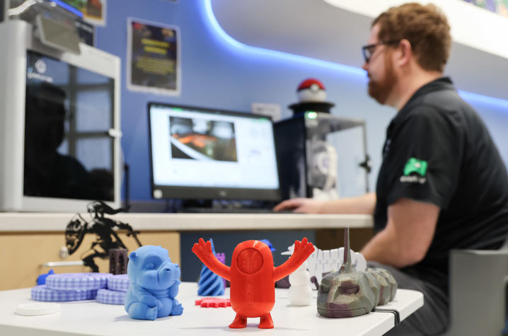 Image of Cody sitting at a computer with 3D printed figures in the foreground