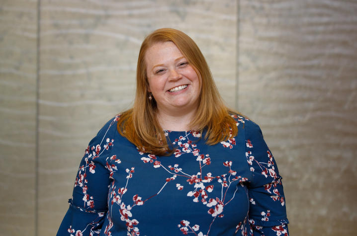 Waist-up photo of Allison Gibson, PhD, assistant professor of social work. She's a white woman in her 30s with straight, strawberry blonde hair that falls past her shoulders. She's smiling at the camera and wearing a blue dress with cherry blossoms on it.