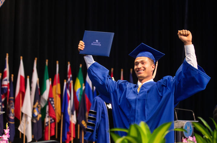 Graduate smiles with arms up in the air while walking across stage