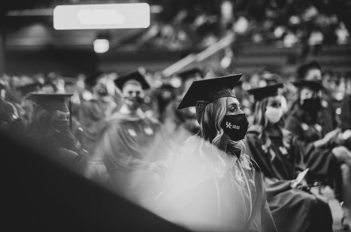 Crowd of graduates seated in caps and gowns on floor of Rupp Arena