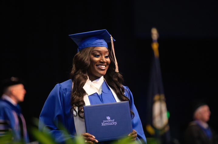 Graduate smiles on stage with diploma cover in hand