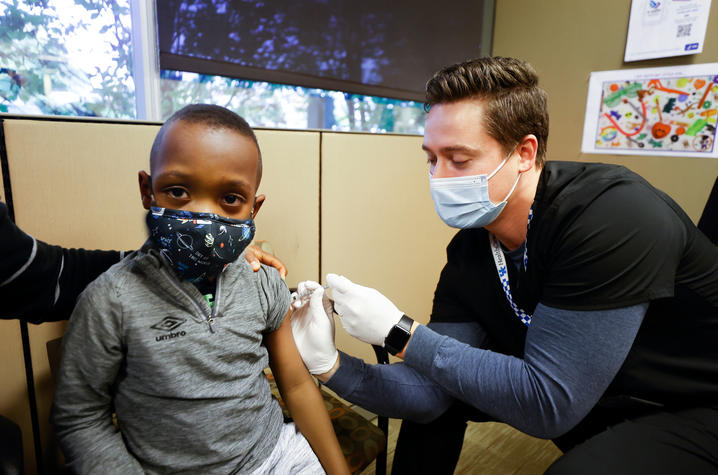 image of a pharmacist demonstrating the COVID-19 vaccine on a young boy.