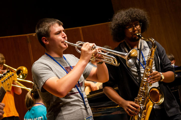 White male playing trumpet and black male playing tenor saxophone.