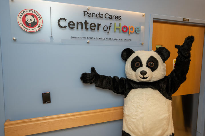 image of a person in a panda costume standing in front of sign for the Panda Cares Center of Hope