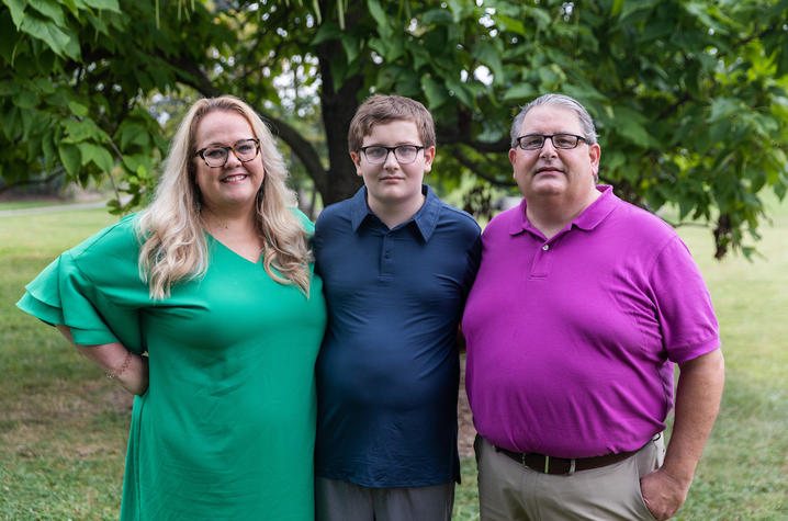 Image of Stephen Wilson in purple shirt, Henry Wilson in navy shirt sitting on a tree branch, and Lori Wilson in green dress