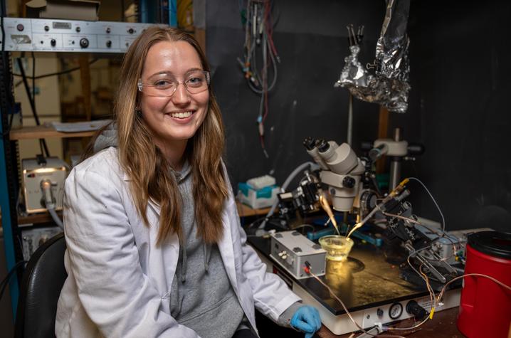 UK student Kaitlyn Brock seated next to a piece of lab equipment