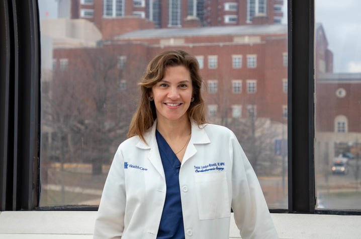 Photo of Tessa London-Bounds image of Dr. London-Bounds in scrubs with white coat standing in long cooridor.