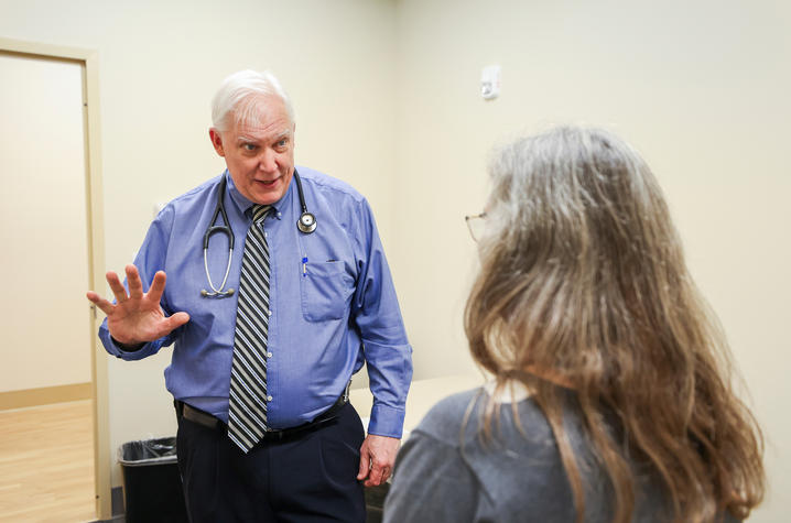Dr. Greg Jicha speaks with a patient A physician wearing a blue shirt, tie and stethoscope gestures while speaking with a seated patient during a clinical visit.