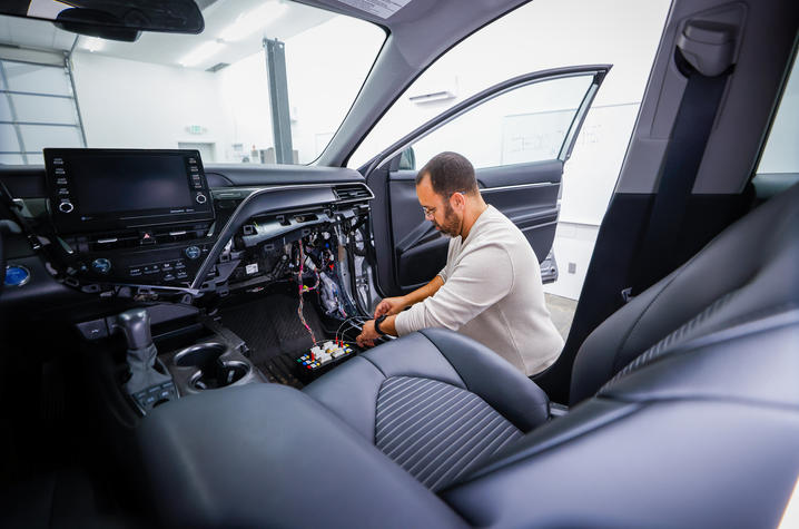 Technician working inside a car, adjusting components beneath the dashboard.