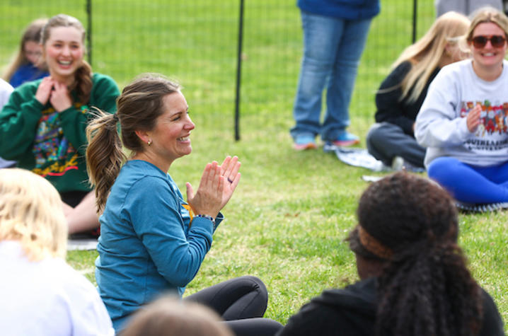 Person seated on grass clapping during an outdoor group yoga session.
