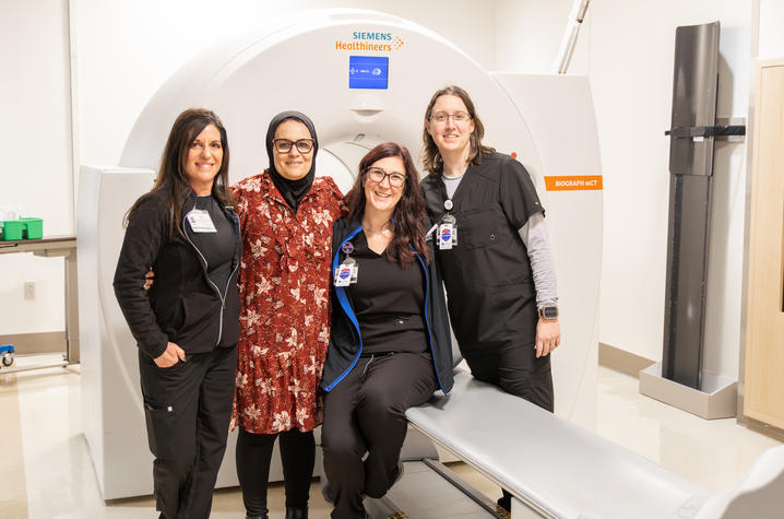 Four women stand and sit together smiling in front of a Siemens Healthineers medical imaging scanner in a clinical setting. 