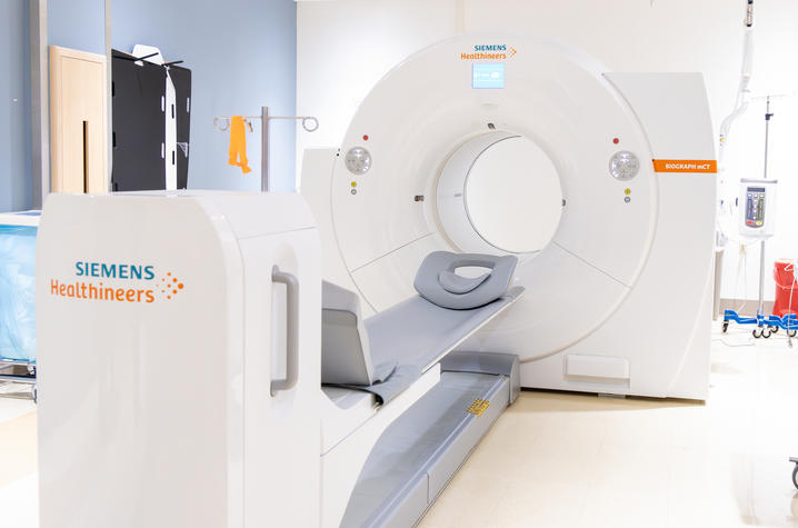A Siemens Healthineers medical imaging scanner with a sliding patient table sits in a bright, clean clinical room. The circular scanner opening and padded table are positioned for a diagnostic imaging procedure.
