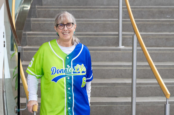 Person on a staircase wearing a bright two-tone baseball jersey in green and blue with ‘Donate Life’ printed across the chest.