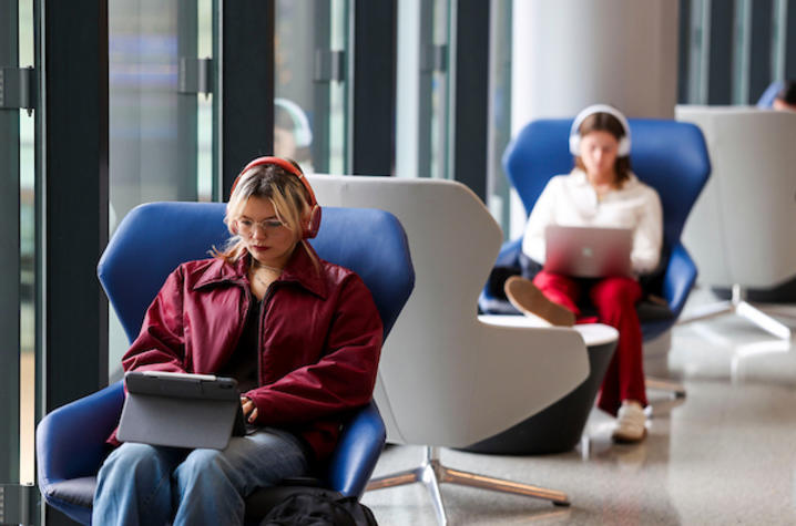 People seated in modern lounge chairs using tablets and laptops in a bright indoor space.