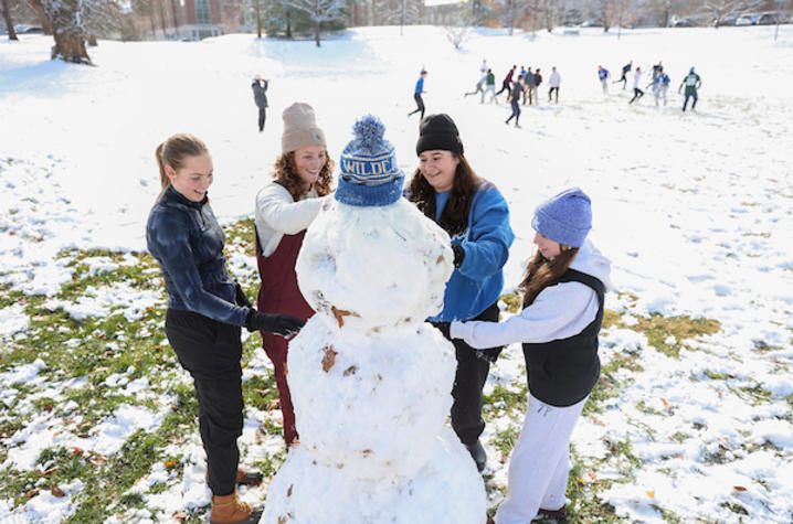 Group of students building a snowman on a snowy campus lawn.