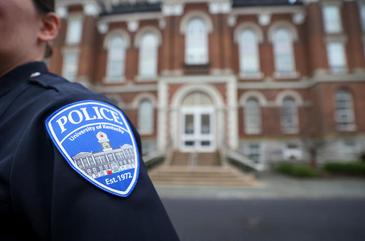 Police uniform with a University of Kentucky Police Department shoulder patch in the foreground, with a campus building blurred in the background.  Provide your feedback on BizChat