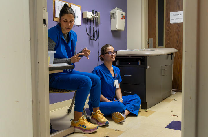 Two nursing students sit on the floor of a clinical skills room, demonstrating and discussing how to identify and treat insect bites during a first aid lesson.