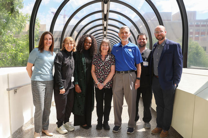 A group portrait of seven people standing in a glass-enclosed pedestrian bridge at UK HealthCare.