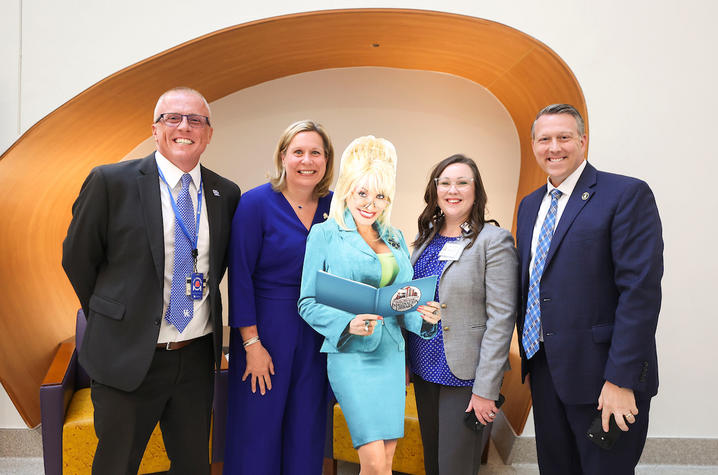Group of adults pose together in a healthcare space around a Dolly Parton standee holding a children’s book.