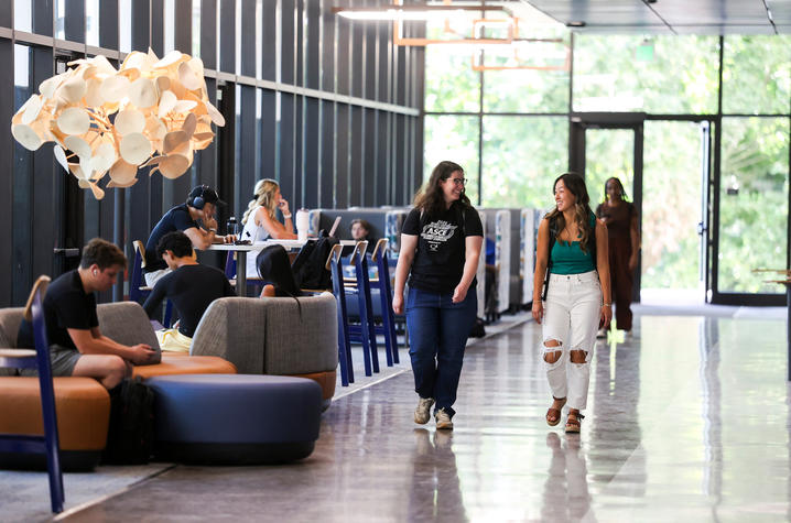 Students study, work, and walk through a bright lounge area inside a campus building.