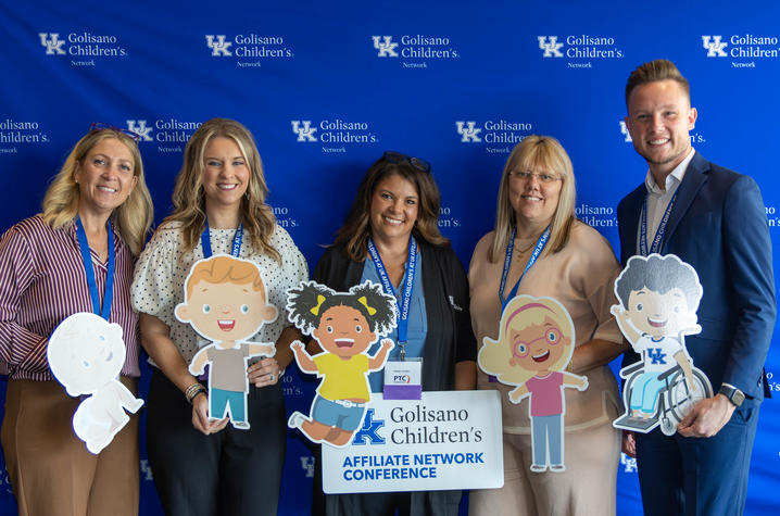 Photo of group at UK Golisano Affilate conference Five conference attendees pose with cartoon child cutouts and an Affiliate Network Conference sign in front of a UK Golisano Children’s Network backdrop.