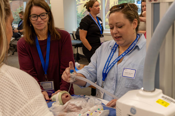 Photo of providers receiving training on neonatal resuscitation People wearing conference badges gather around a medical training mannequin as one person demonstrates a procedure in a clinical simulation lab.