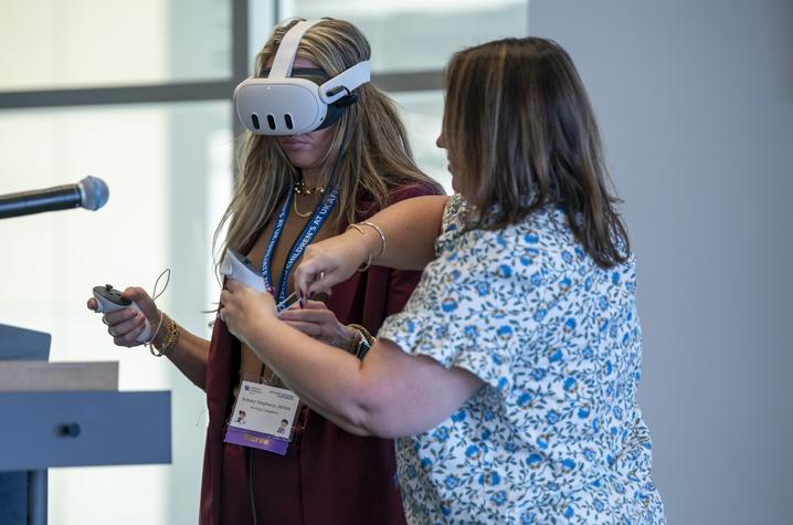 photo of conference attendee using VR in training A conference attendee uses a virtual reality headset while another participant assists during an interactive training session.