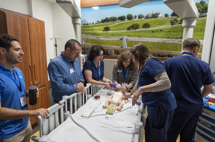 Photo of providers receiving neonatal training Conference attendees participate in a pediatric simulation training exercise around a child-sized mannequin in a hospital room setting.