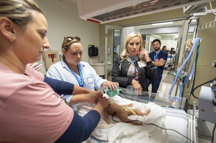 Photo of providers receiving training on neonatal resuscitation Conference attendees participate in a neonatal simulation training exercise, using respiratory equipment on an infant mannequin in a hospital care setting.