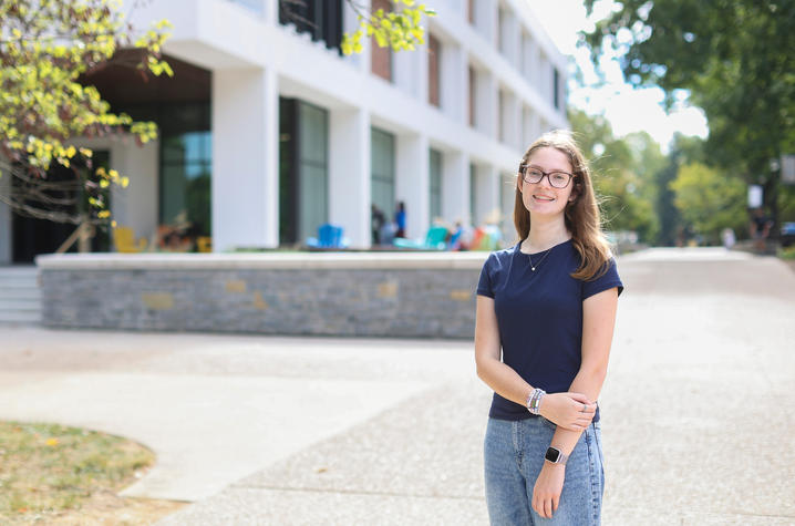 Person standing on a campus walkway in front of a modern academic building.