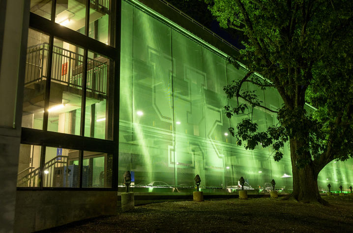 UK goes green Exterior view of a multi-story building illuminated with bright green lighting at night. A large translucent green facade stretches along the structure, while an adjacent glass stairwell reveals interior landings and railings.
