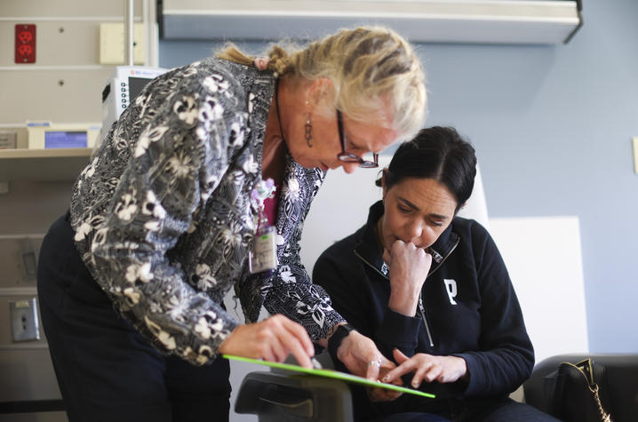 Two people look down together at a document on a green clipboard in a clinical exam room.
