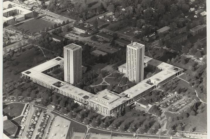 Black-and-white aerial photograph of a large modernist complex featuring two tall rectangular towers, connected low-rise buildings, landscaped grounds, and surrounding parking lots and neighborhoods.