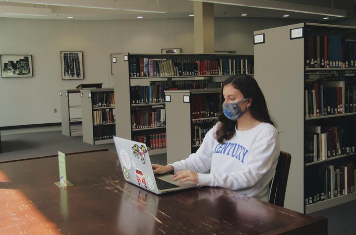 photo of masked student working on laptop in library