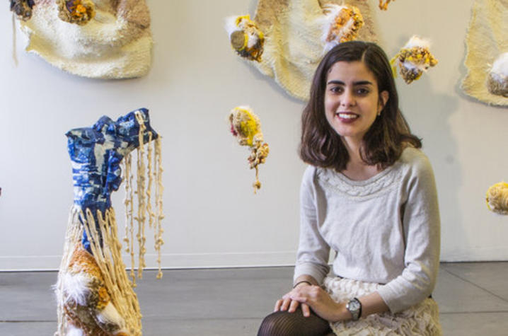 photo of Amalia Galdona Broche seated in gallery with her art surrounding her