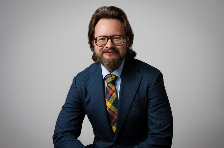 photo of Andrew Pilny Person wearing glasses and a blue suit with a patterned tie sits against a neutral background, facing the camera.